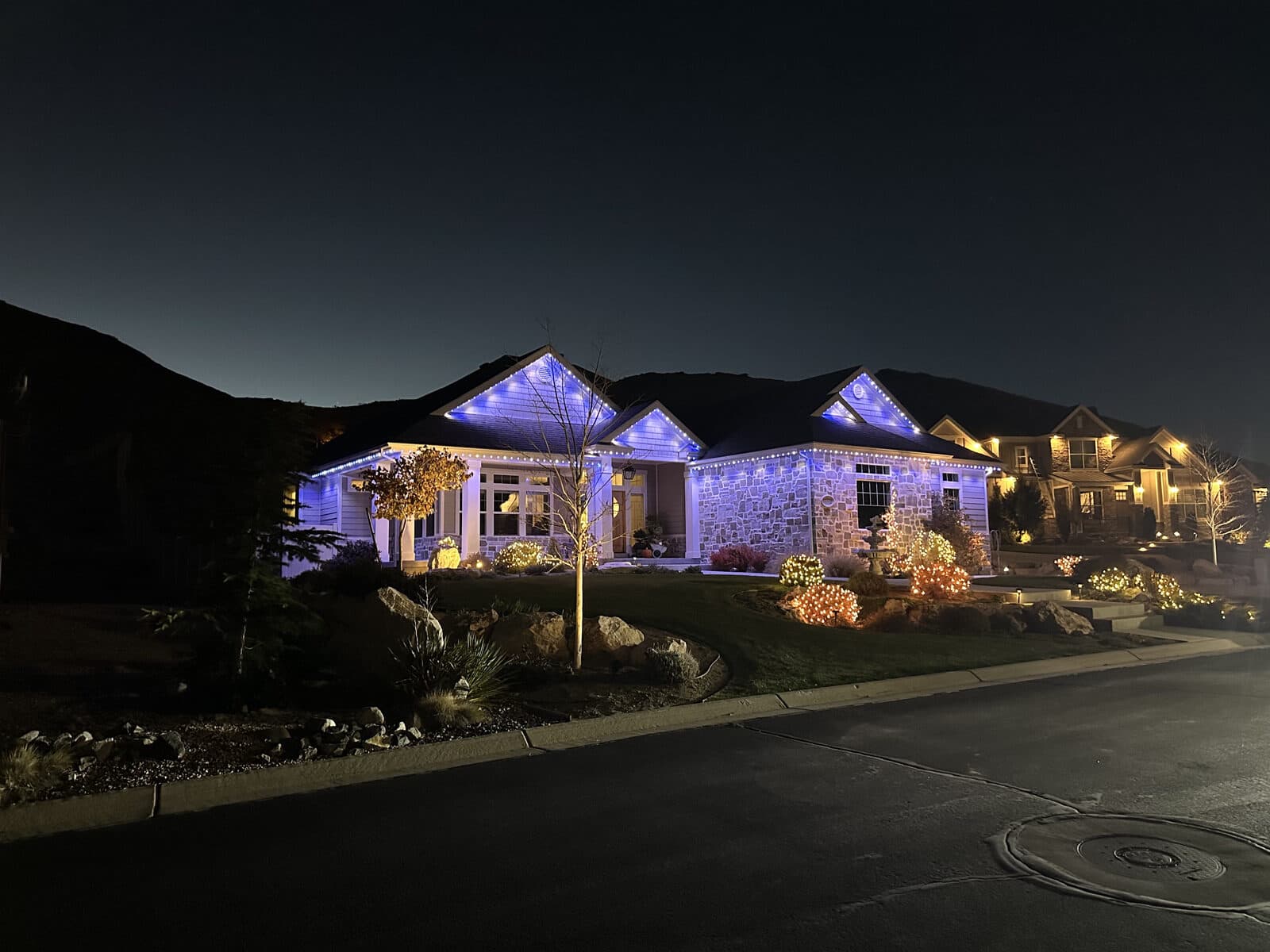 Real Alta permanent lighting install in blue and white on a Utah stone rambler at blue hour